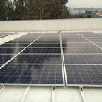 Rooftop solar panel installation showing multiple mounted photovoltaic panels secured with white aluminum rails and red clamp