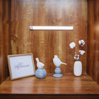 LED under-cabinet light displayed on wooden shelf with decorative bird figurines, framed airplane sketch, and cotton stems in