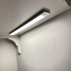 Slim LED under-cabinet light mounted on white kitchen cabinetry, emitting bright white illumination across the wall below.