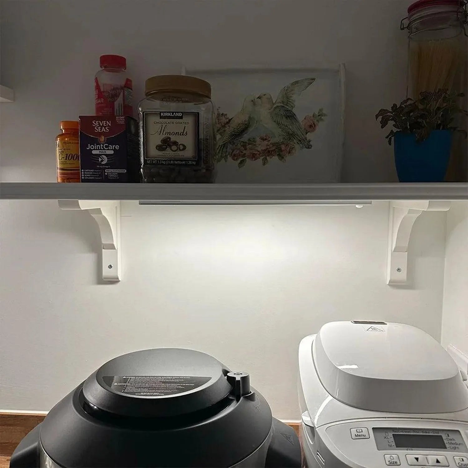 White LED under-cabinet light installed below bathroom shelf holding vitamins and almonds.