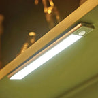 LED under-cabinet light installed on kitchen cabinet edge, illuminated with bright white light and motion sensor visible.