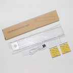 LED motion sensor light unboxed showing white under-cabinet fixture, USB cable, instruction manual, and adhesive mounting str