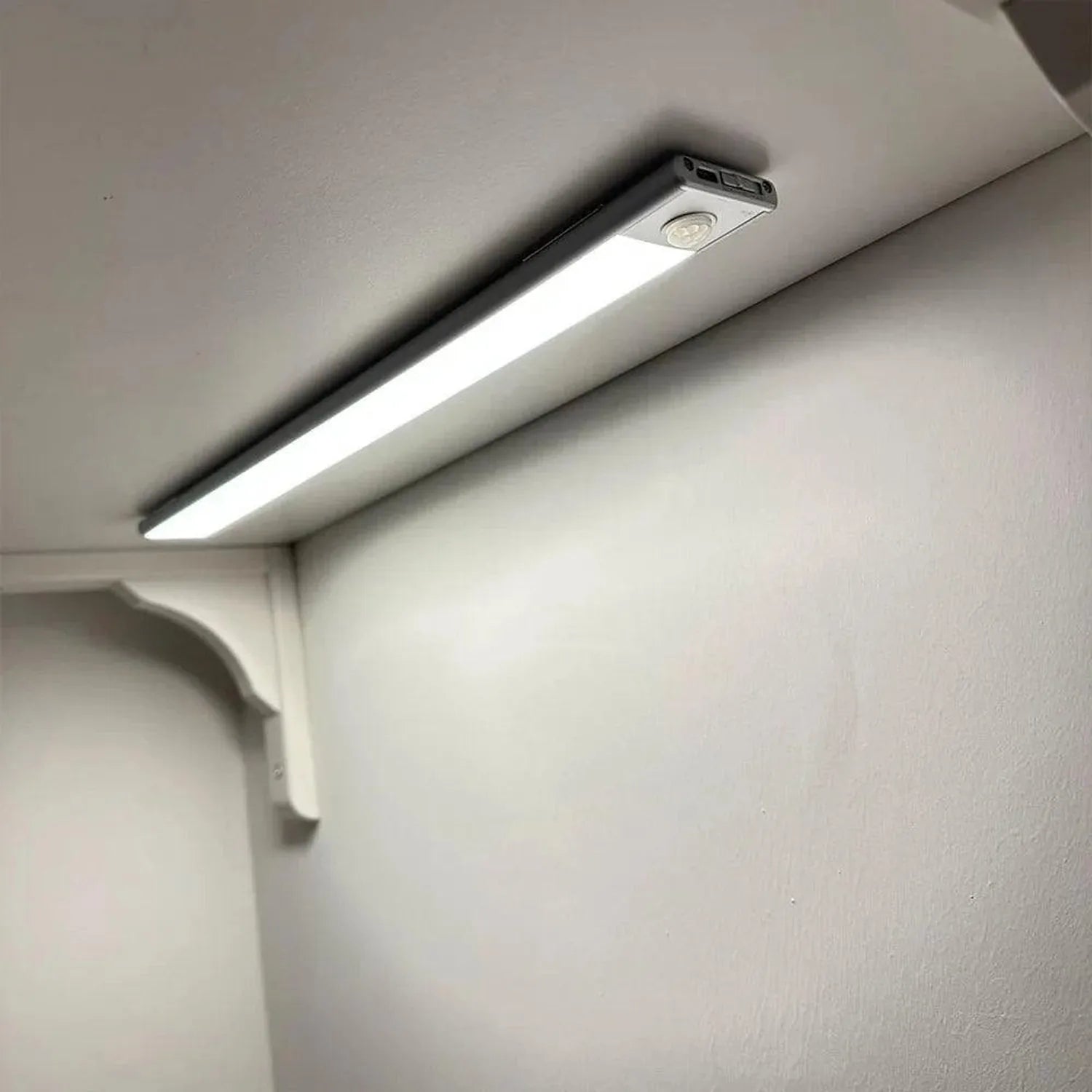 White LED under-cabinet light mounted on ceiling, glowing brightly above a wall surface, installation shot.