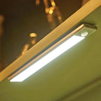 Motion-sensor LED under-cabinet light installed beneath wooden shelf, emitting bright white light against green wall backgrou