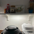 White LED under-cabinet light installed below kitchen shelf with almonds jar and supplements visible above.