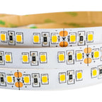 Coiled LED strip light showing yellow SMD diodes, resistors, and cut marks on white flexible PCB backing.