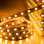 Warm white LED strip light coiled in loops, showing individual LED modules and circuit board details against golden-lit backg