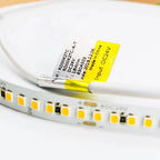 Close-up of yellow LED strip label with specifications attached to coiled white flexible strip with yellow LED diodes.