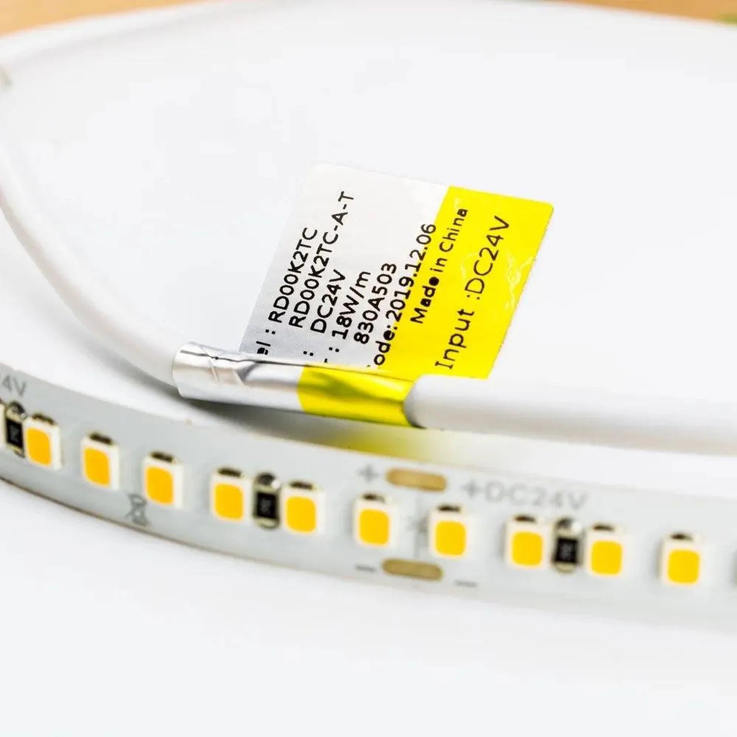 Close-up of yellow LED strip label with specifications attached to coiled white flexible strip with yellow LED diodes.