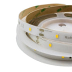 Rolled LED light strips with yellow SMD chips on white backing, labeled +DC24V and RoHS compliant, tan adhesive side visible.