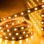 Warm white LED strip light coiled in loops, showing individual diodes on flexible circuit board against yellow-lit background