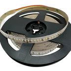 Coiled LED strip light on black reel showing warm white SMD LEDs, 24V connection points, and rainbow-striped adhesive tape ba