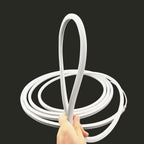 Hand holding white LED neon flex strip light coiled in loops against dark background, product display shot.