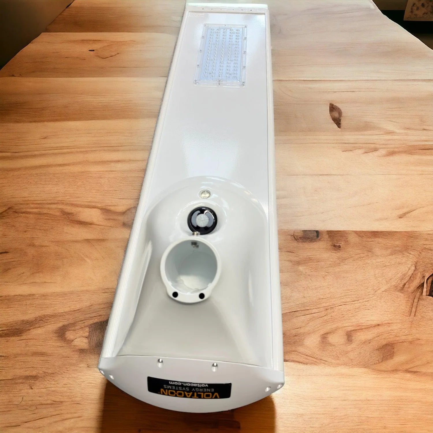 White solar LED street light viewed from above on wooden floor, showing panel, motion sensor, and battery compartment.