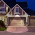 Sunforce solar security light mounted above garage door on residential home at dusk, illuminating driveway and garage doors.