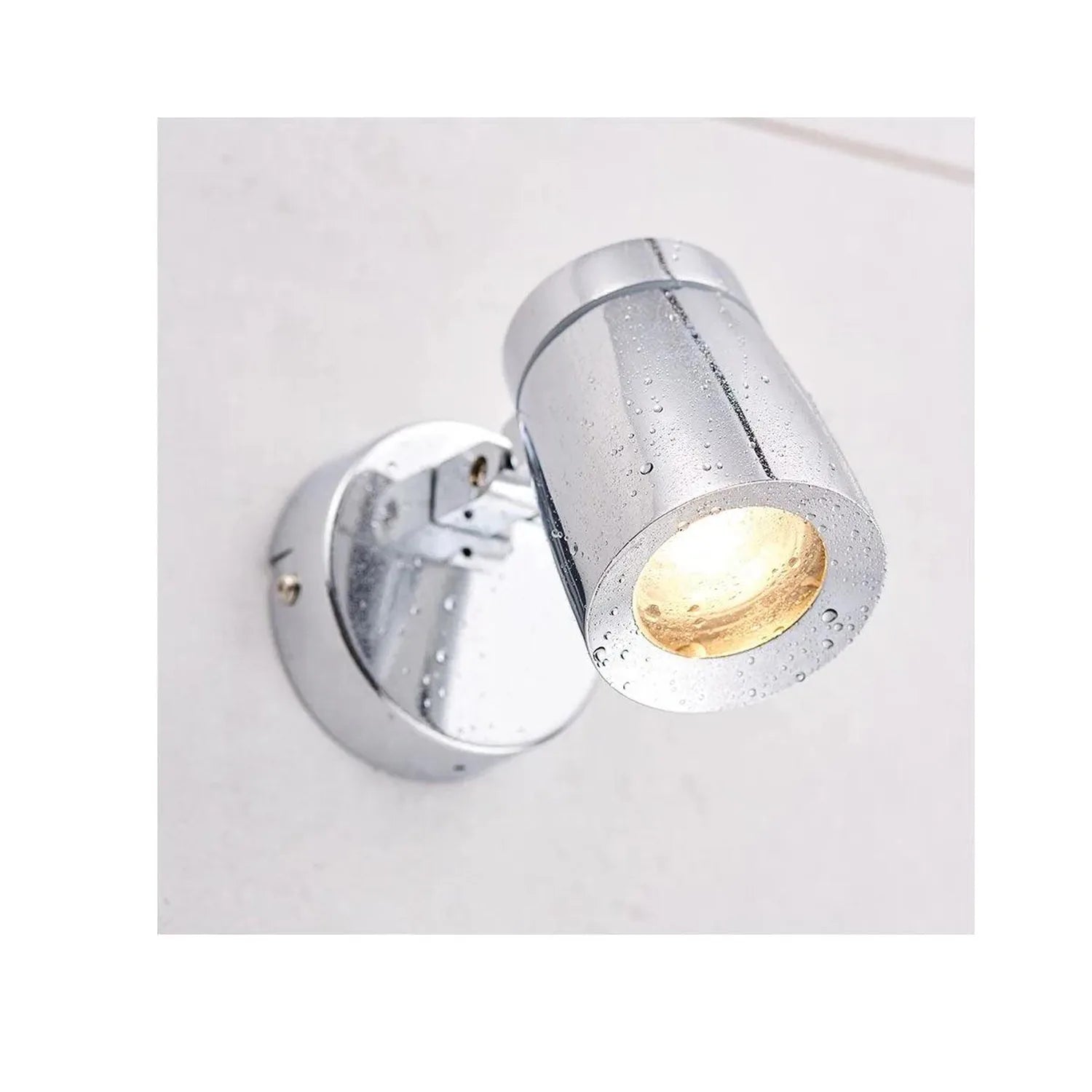 Polished chrome cylindrical LED bathroom spotlight mounted on white wall, angled downward with warm light glowing from openin