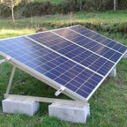 Adjustable solar panel mounting bracket installed outdoors on grass, supporting multiple blue solar panels at an angled posit