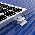 White mounting pad with bolt holes securing solar panel to blue corrugated metal roof, installation shot.