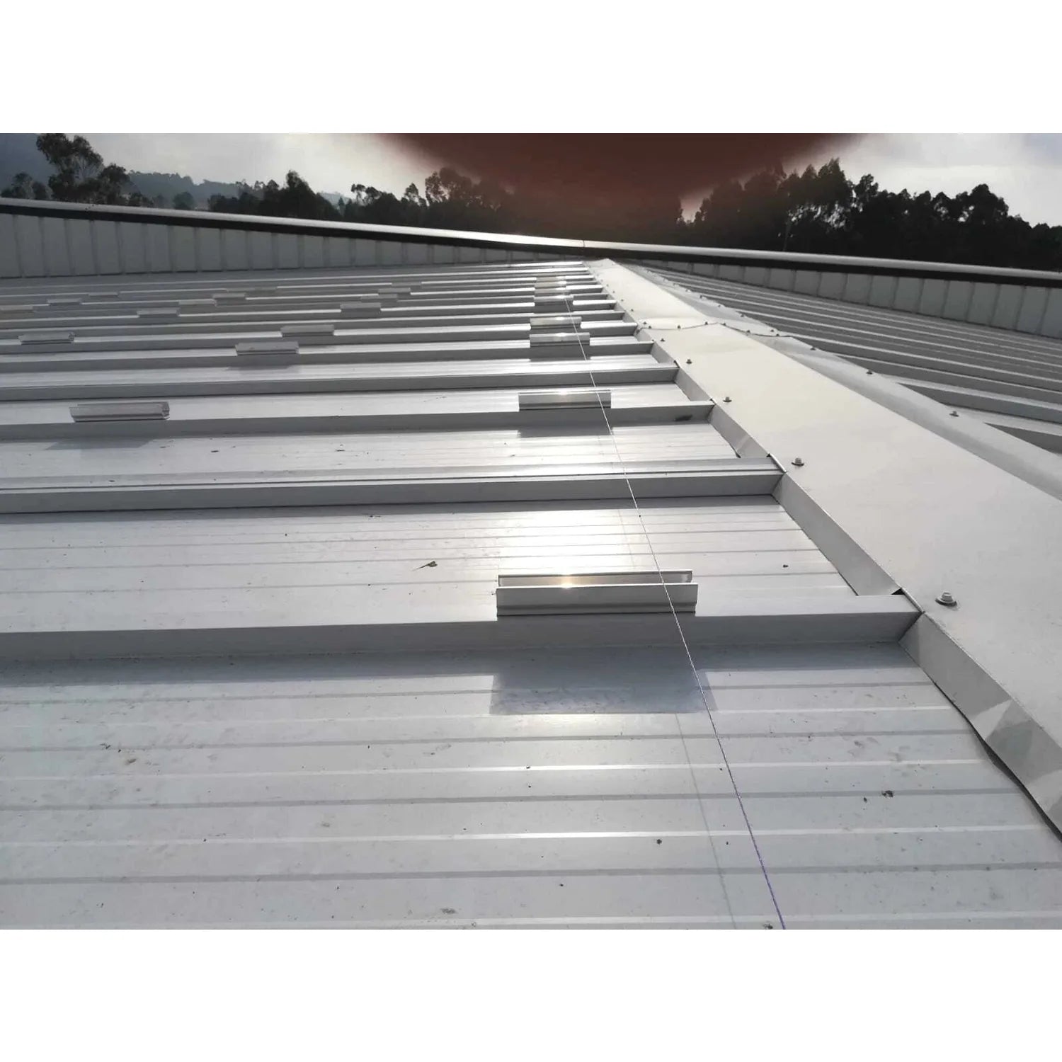 No-Drill Solar Panel Mounting Kit installed on flat metal roof with bonded rails and cable management system, forested backgr