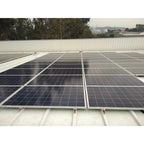 Solar panels mounted on corrugated metal roof using bonded rail system, rural landscape with trees in background.