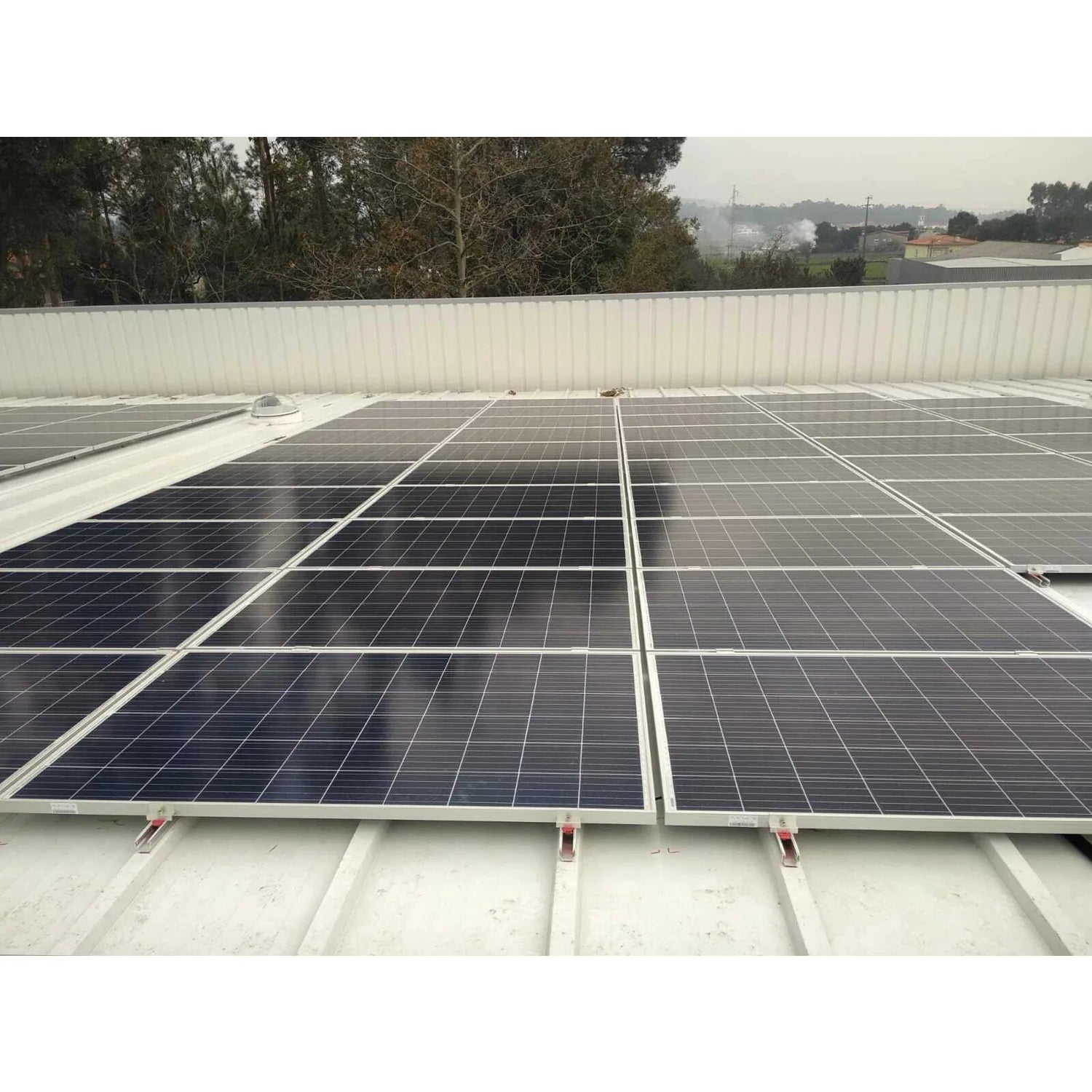 Solar panels mounted on corrugated metal roof using bonded rail system, rural landscape with trees in background.