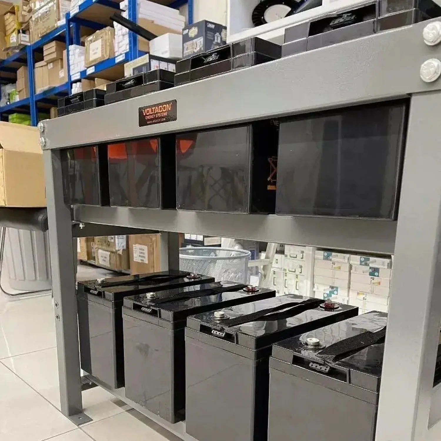 Voltacon display unit showing eight 6V 200Ah gel batteries arranged in rows, installed in warehouse setting with shelving vis