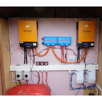 Solar energy system installation with two Voltagon inverters, blue charge controllers, and safety disconnects mounted on pink