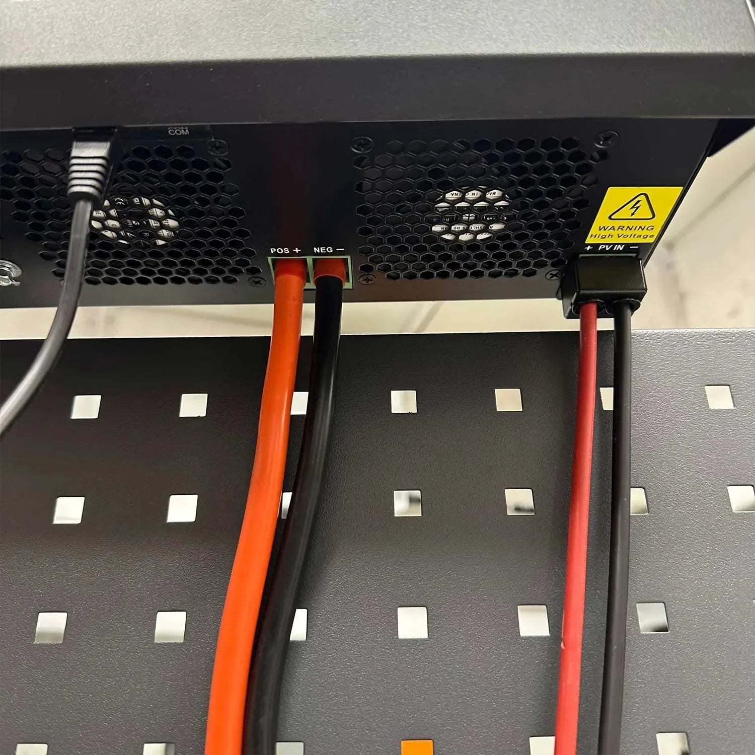 Close-up of solar inverter rear panel showing positive and negative terminal connections with orange and black cables, high v