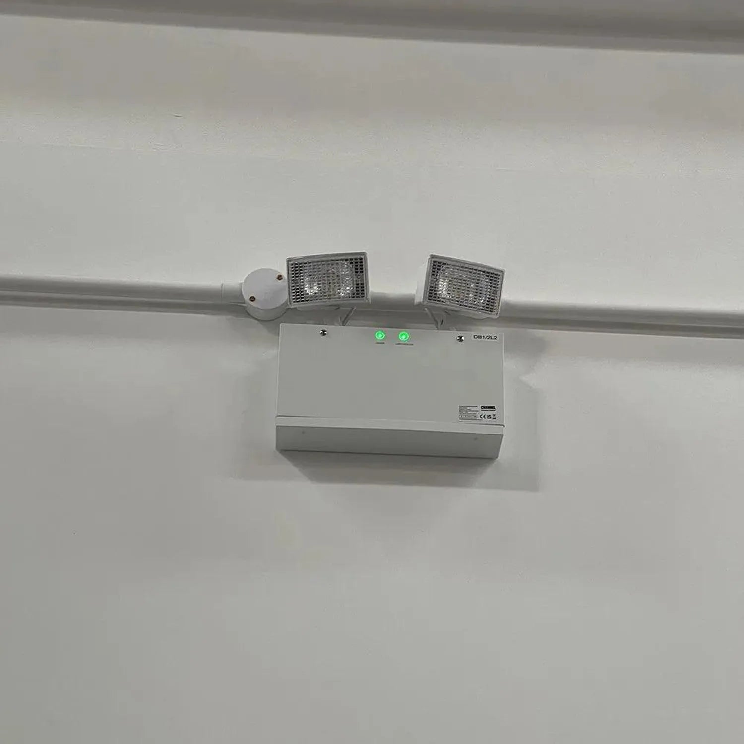 White ceiling-mounted emergency light unit with twin LED spotlights and motion sensor, installed against white ceiling.