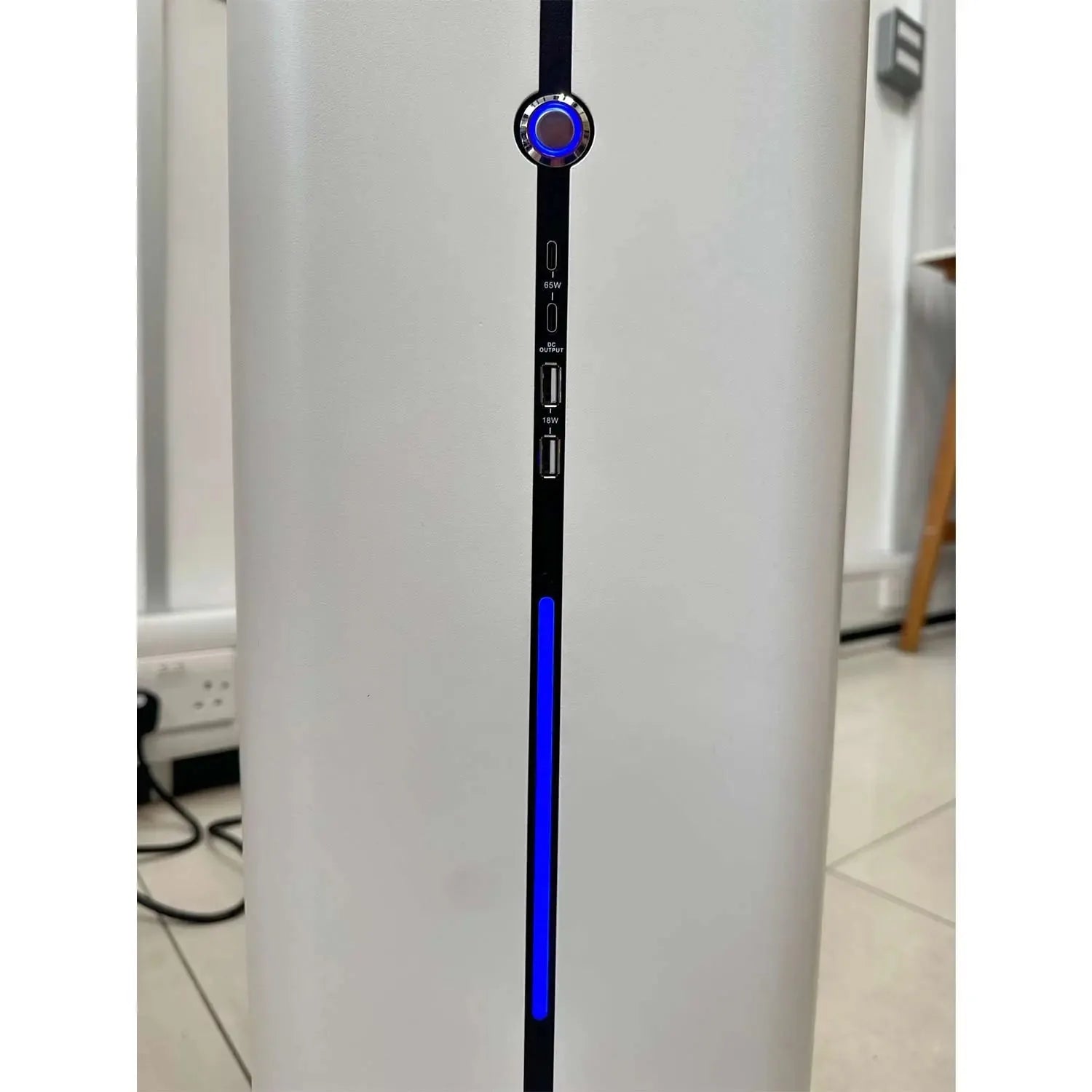White cylindrical power station with blue LED strip and illuminated power button, shown in installation shot against white wa