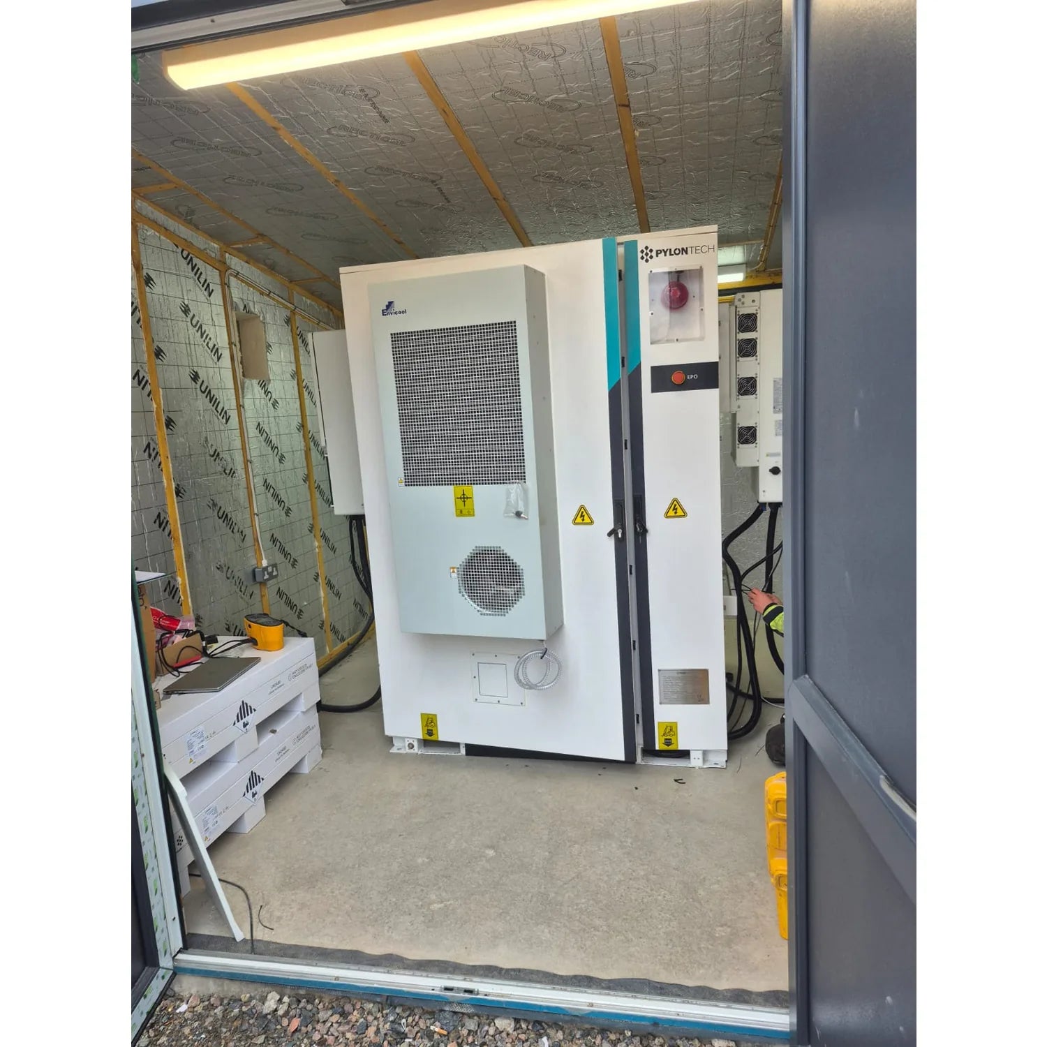 Pylontech battery storage system installed in industrial container with cooling unit, electrical panels, and safety warning l