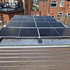 Solar panel array installed on flat roof with integrated mini rail ballast system, residential brick building backdrop.
