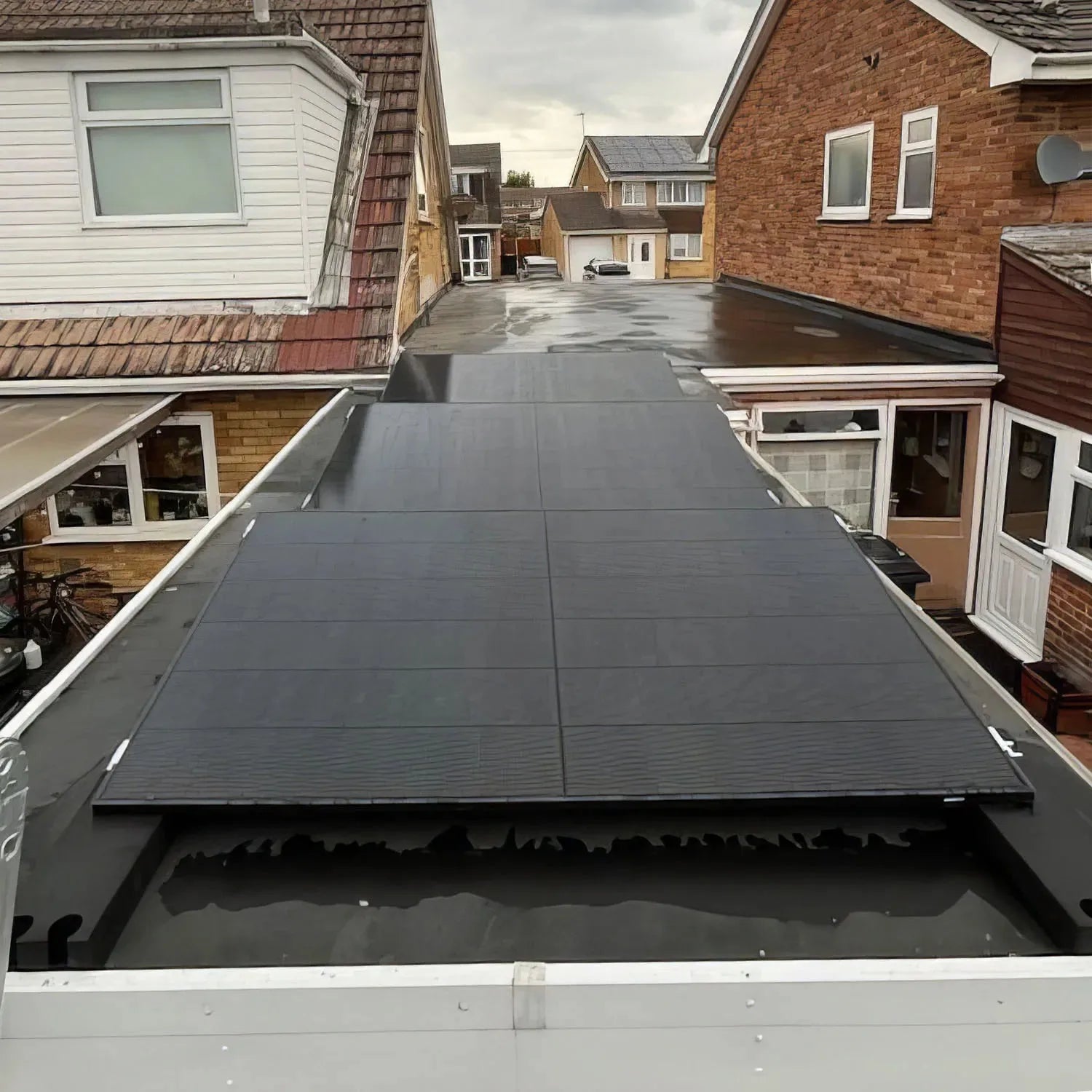 Solar panel mounting system installed on residential flat roof between brick houses, angled southward.