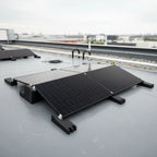Black dual-panel solar mounting system installed on industrial flat roof with ballast feet and cable connections visible.