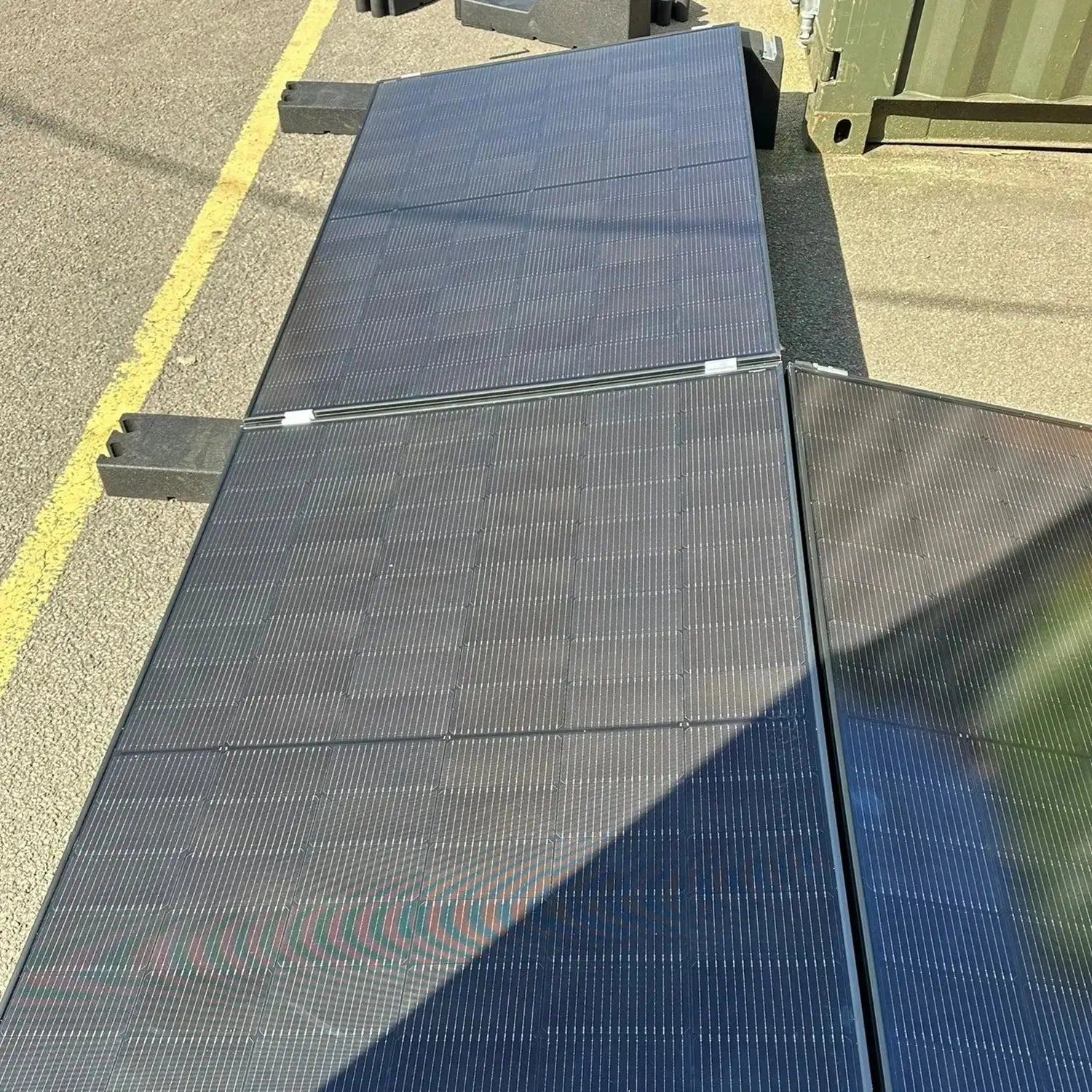 Solar panel array mounted on flat roof with angled brackets, showing multiple connected panels in sunlight with yellow safety