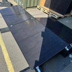 Multiple black solar panels mounted on flat roof system with east-west orientation, displayed outdoors in installation settin
