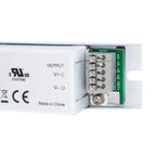 White plastic power supply unit with exposed green circuit board and terminal blocks labeled OUTPUT with V+ and V- connection
