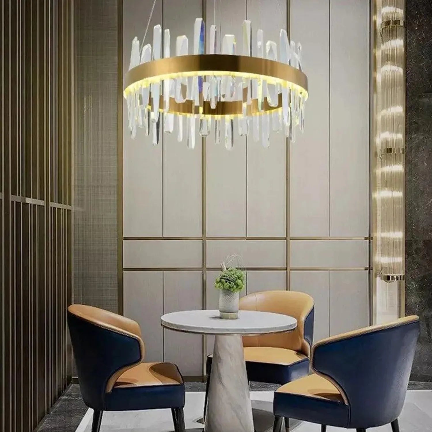 Gold ring pendant light with white crystal rods hanging above round marble table and two navy blue chairs in modern interior 