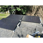 Flat roof solar mounting kit installed on concrete roof with three black solar panels angled east-west, white ballast blocks,