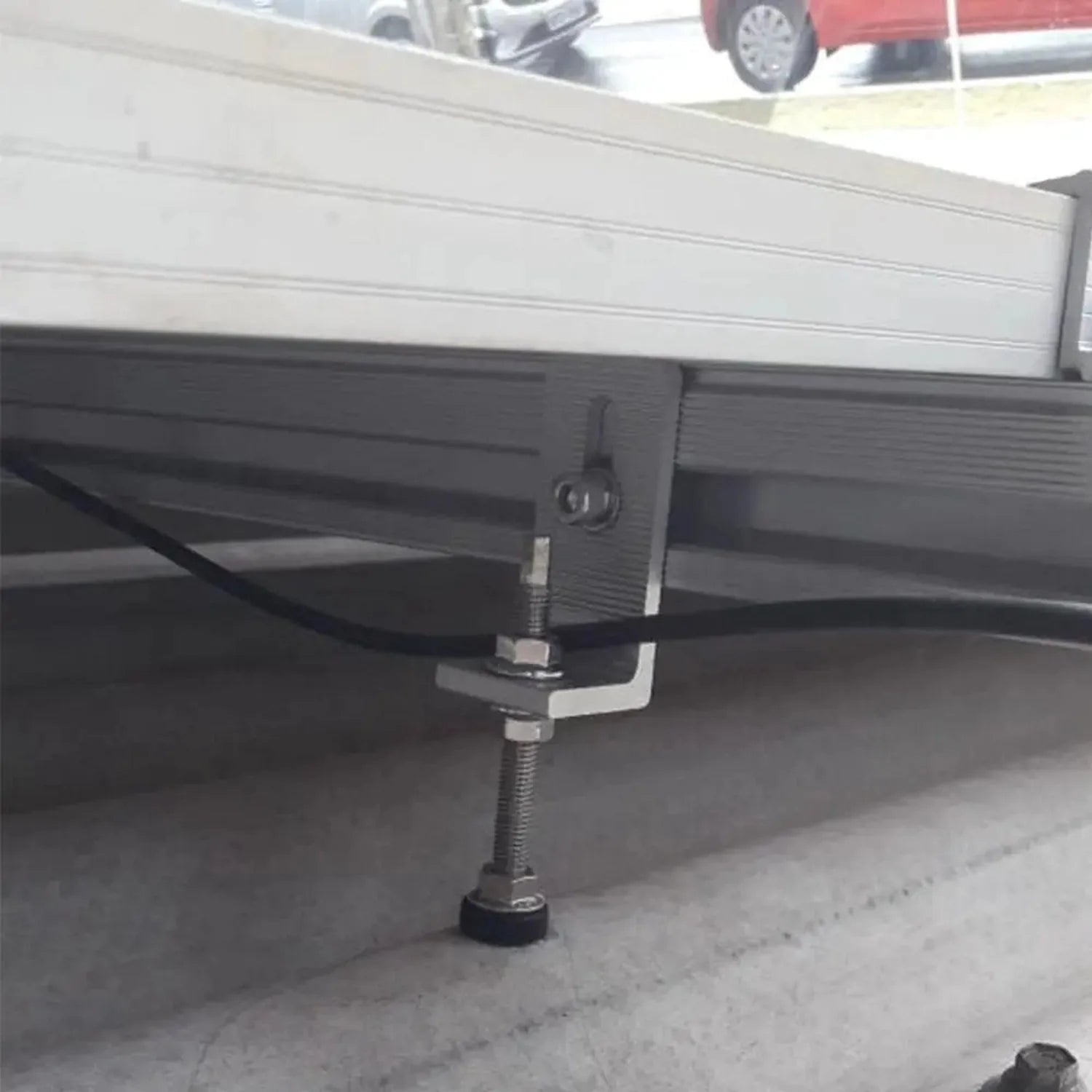 Hanger bolt with supporting plate installed under truck bed, showing threaded bolt and metal bracket attachment in driveway.