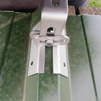 White adjustable solar panel mounting bracket installed on green trapezoidal metal roof panels with adjustment lever visible.