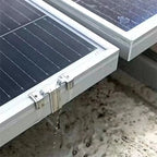 Stainless steel water drain clip mounted on solar panel frame with water droplets flowing downward into sand.