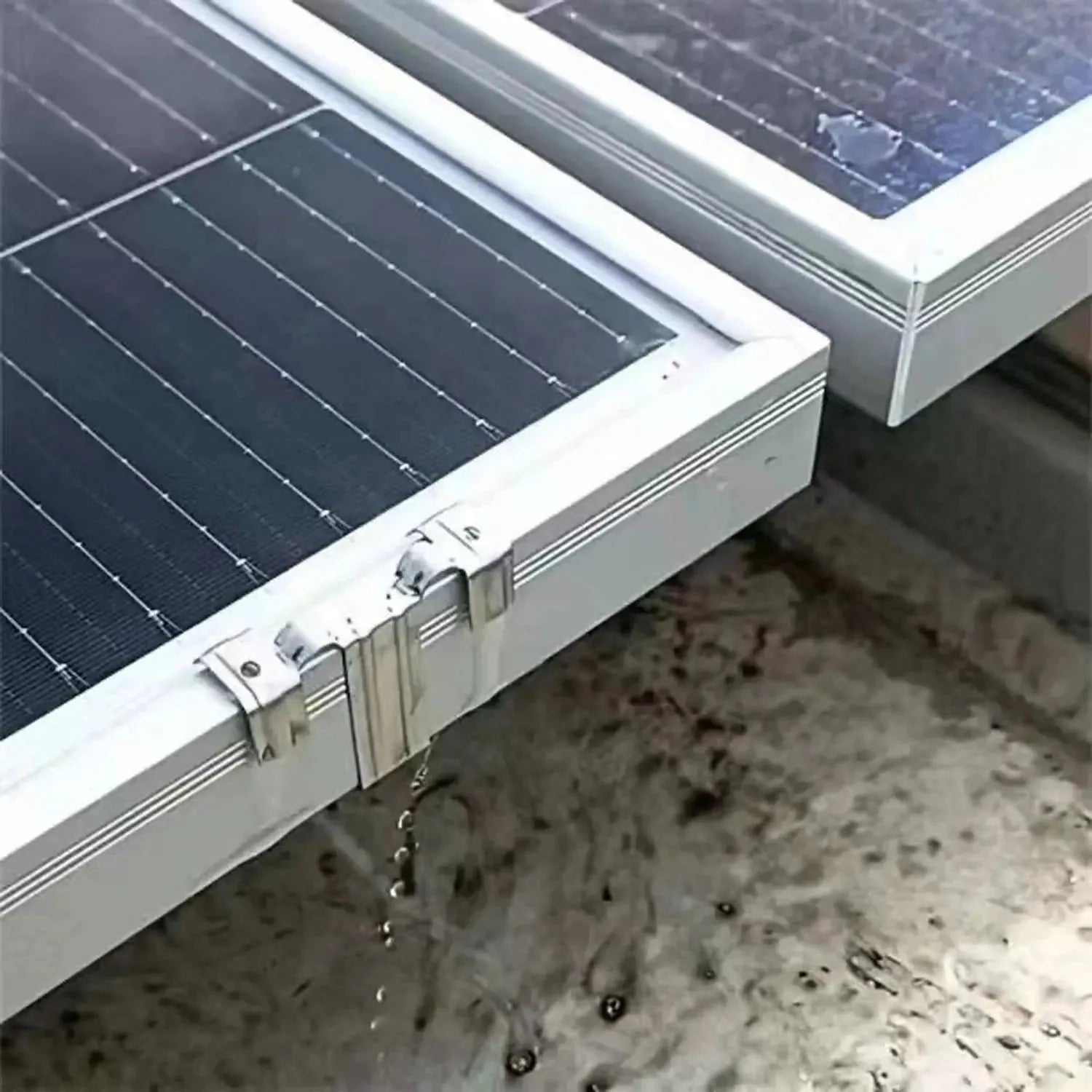 Stainless steel water drain clip mounted on solar panel frame with water droplets flowing downward into sand.