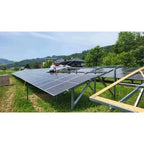 Installation shot of ground-mounted bifacial solar panels in a rural setting with technician on roof and forested hills in ba