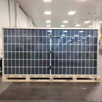 Large solar panel with white frame mounted on wooden pallet in showroom, displaying dark blue photovoltaic cells in grid patt