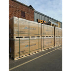 Stacked wooden pallets of JA Solar panels wrapped in plastic, loaded outside a warehouse with VOLTA signage visible above.