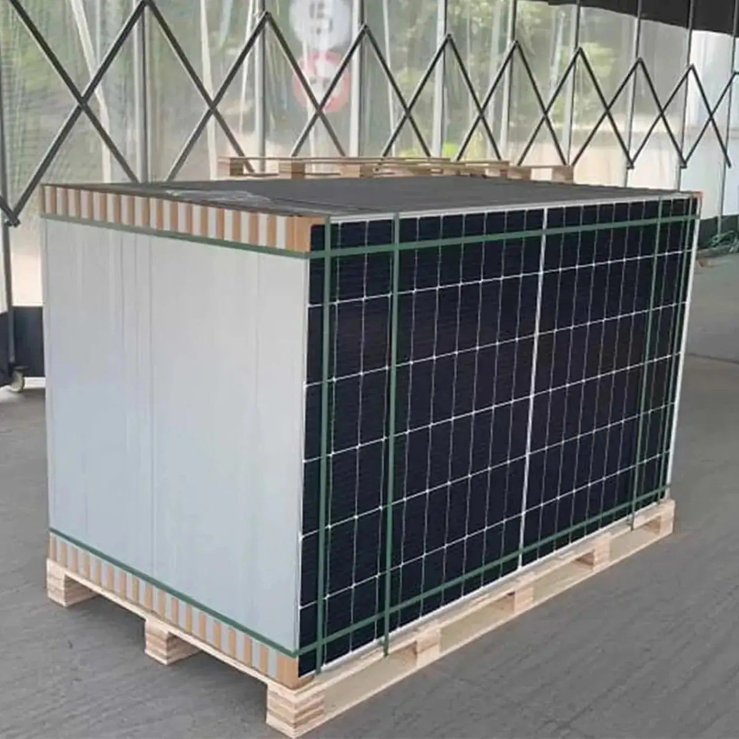 JA Solar 600W bifacial solar panel mounted on wooden pallet with green protective fencing, displayed indoors.