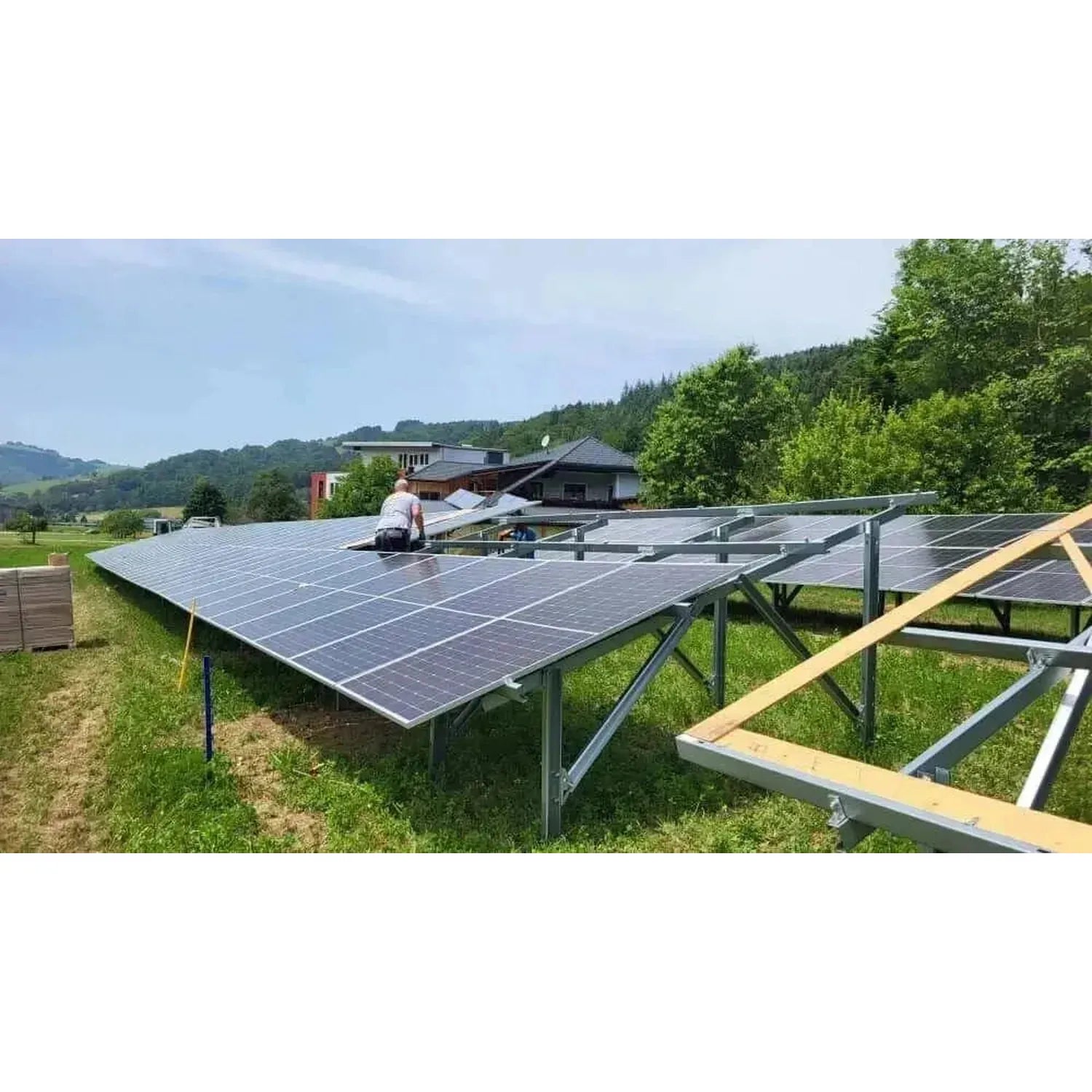 Installation shot of solar panels on ground-mounted racking system in rural hillside setting with technician working on array