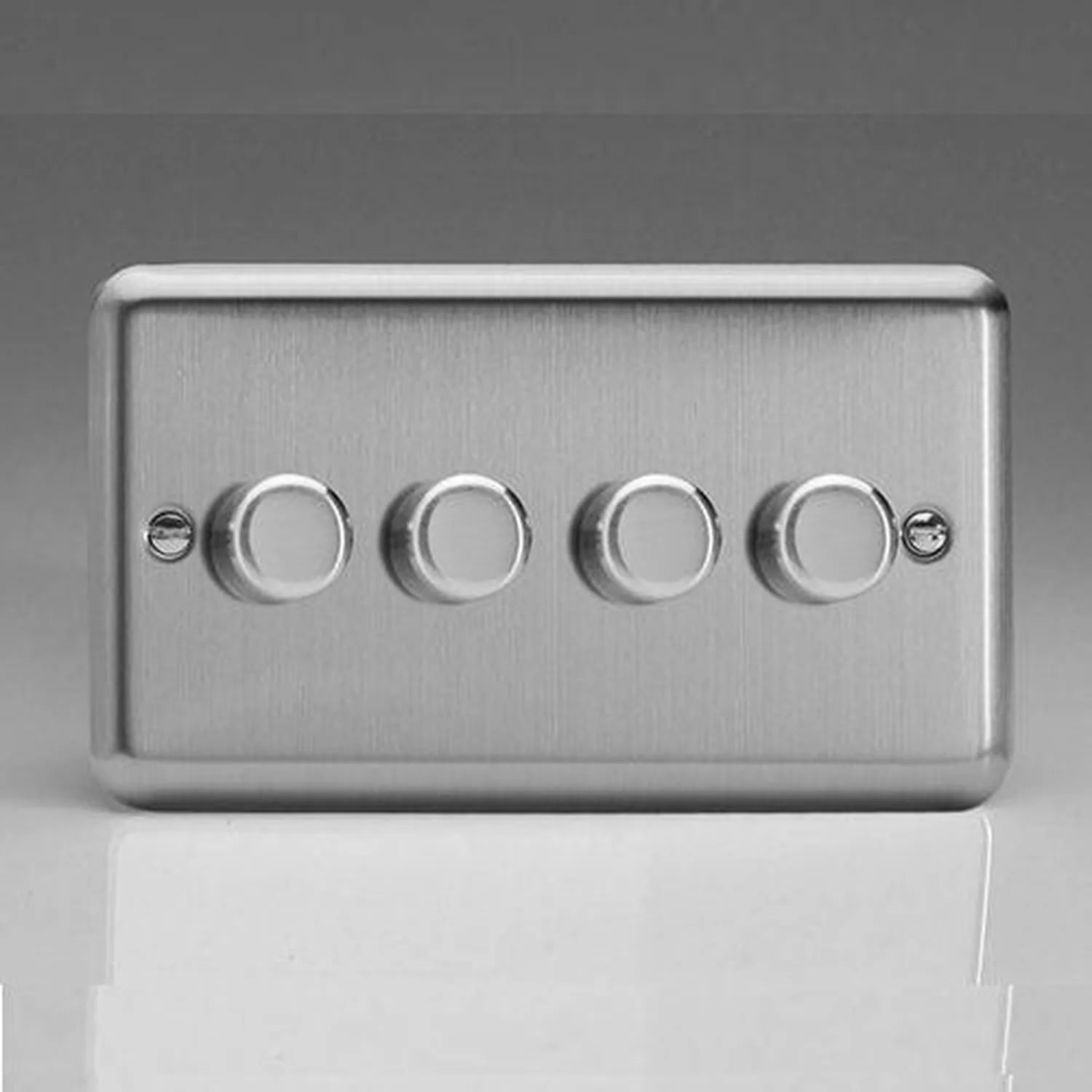 Four-gang brushed steel dimmer switch with rotary controls against gray background.