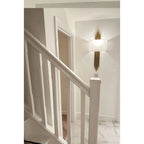 Gold vertical ribbed wall sconce with white shade mounted in modern stairwell hallway.